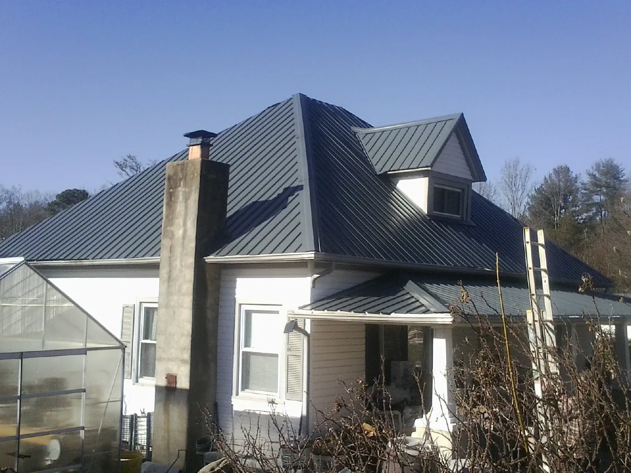 Dark blue standing seam metal roof on a white farmhouse with dormer — Slate & Tile Roof Repair by Roofing Brothers in Grimesland