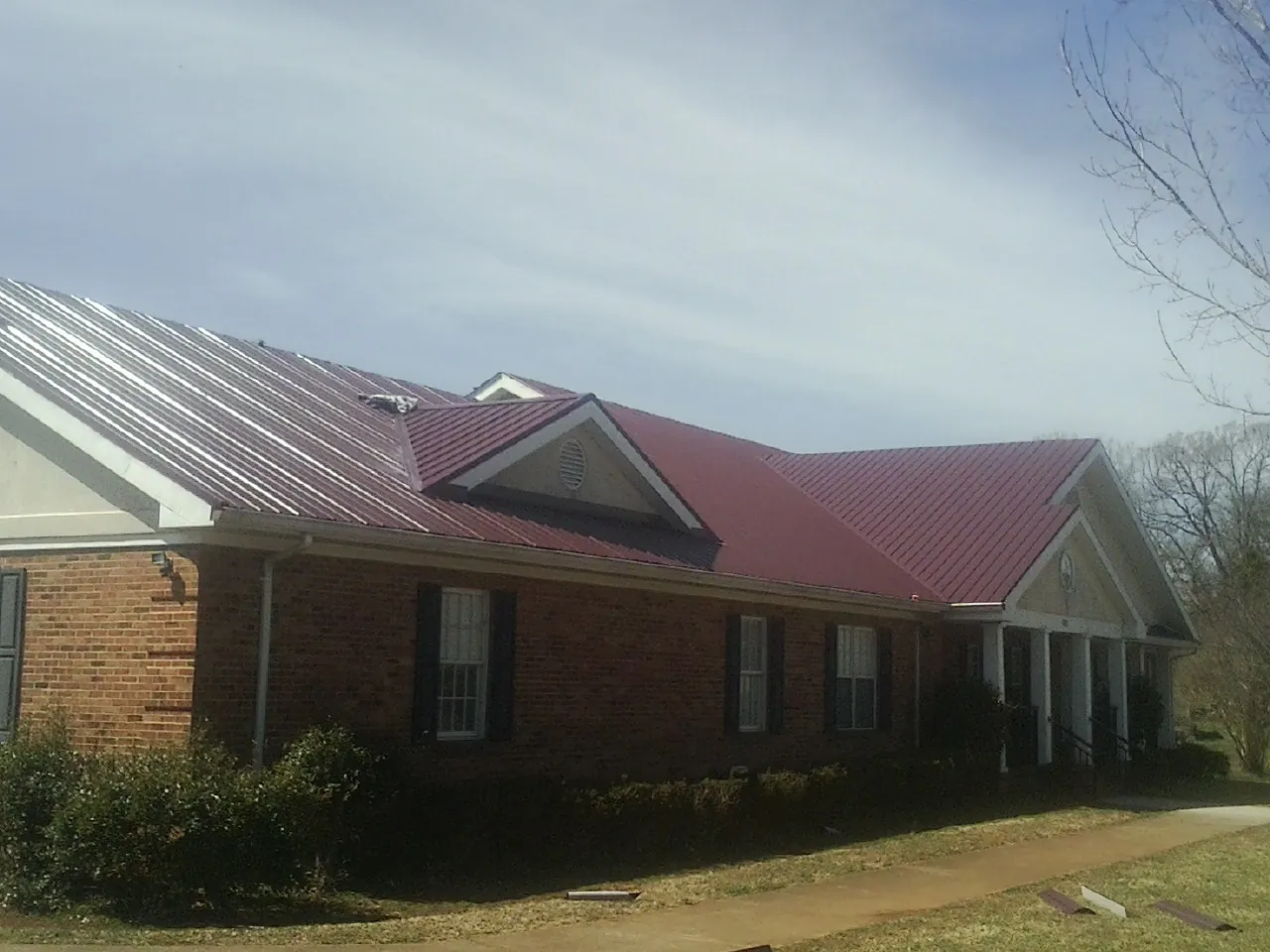 Red metal roof with gabled entries on a long brick building, from a Hail Damage Roof Repair job in Grimesland