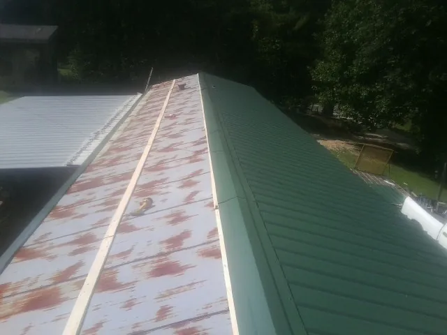 Old rusted panels beside newly installed green metal roofing — Wind Damage Roof Repair by Roofing Brothers in Grimesland