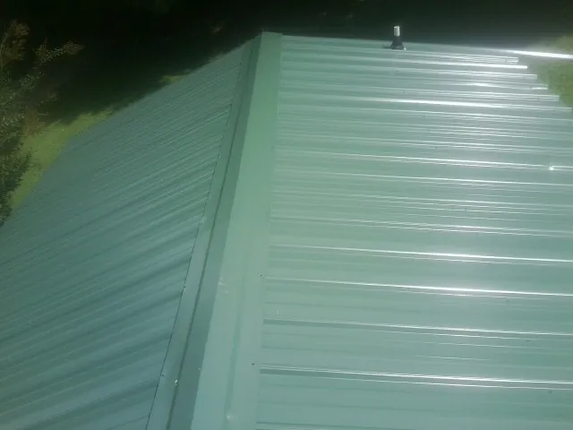 New green metal panels meeting at the ridge of a roof — Flat Roof Repair work by our crew in Grimesland