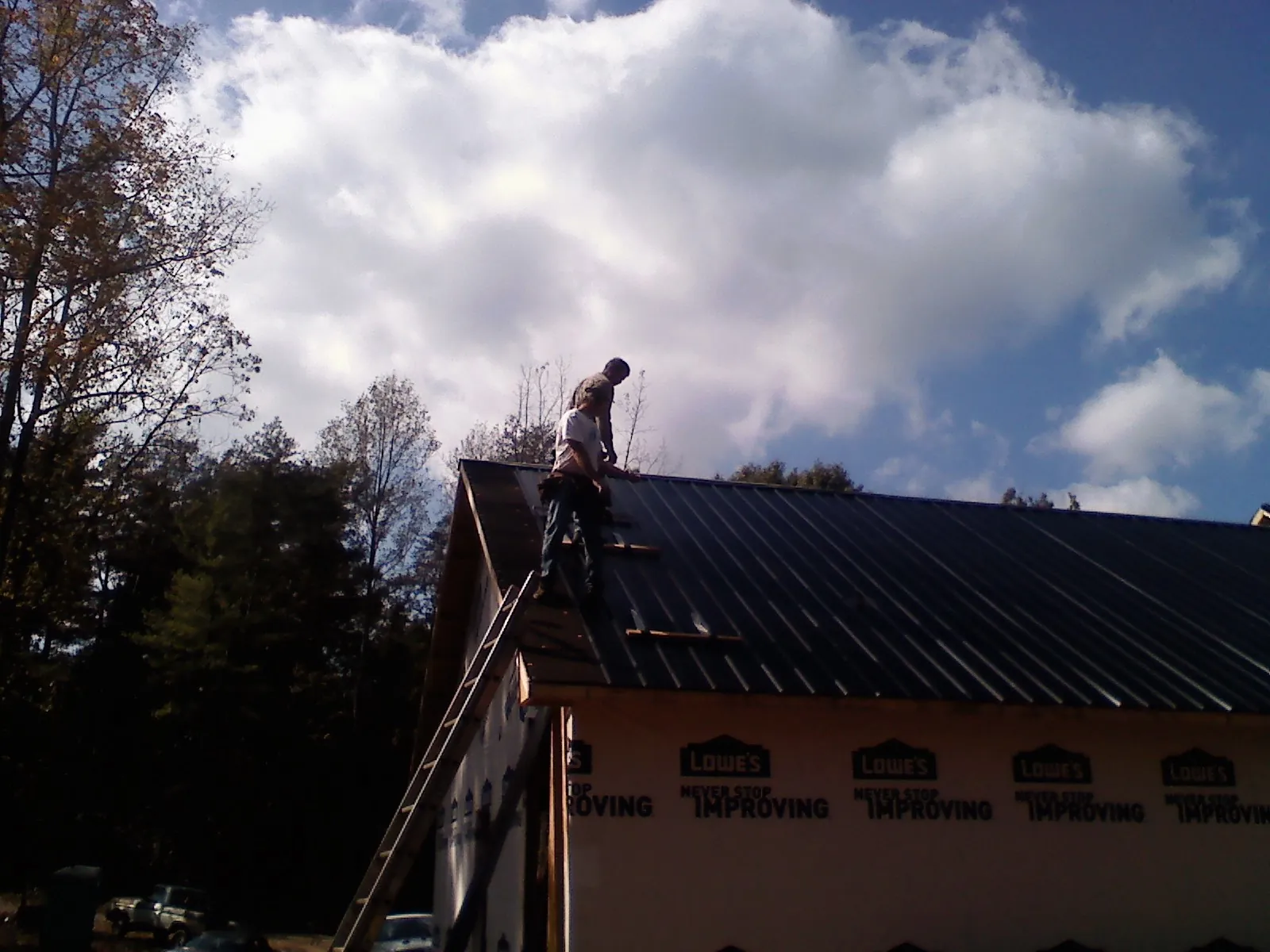 Roofer fastening dark metal panels high against a cloudy sky, from a Roof Inspection job in Grimesland