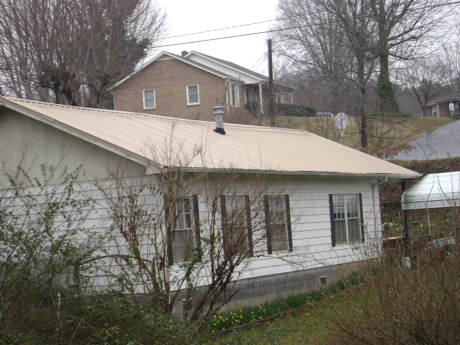 Tan metal roof on a white sided house set into a hillside — Commercial Roofing by Roofing Brothers in Grimesland