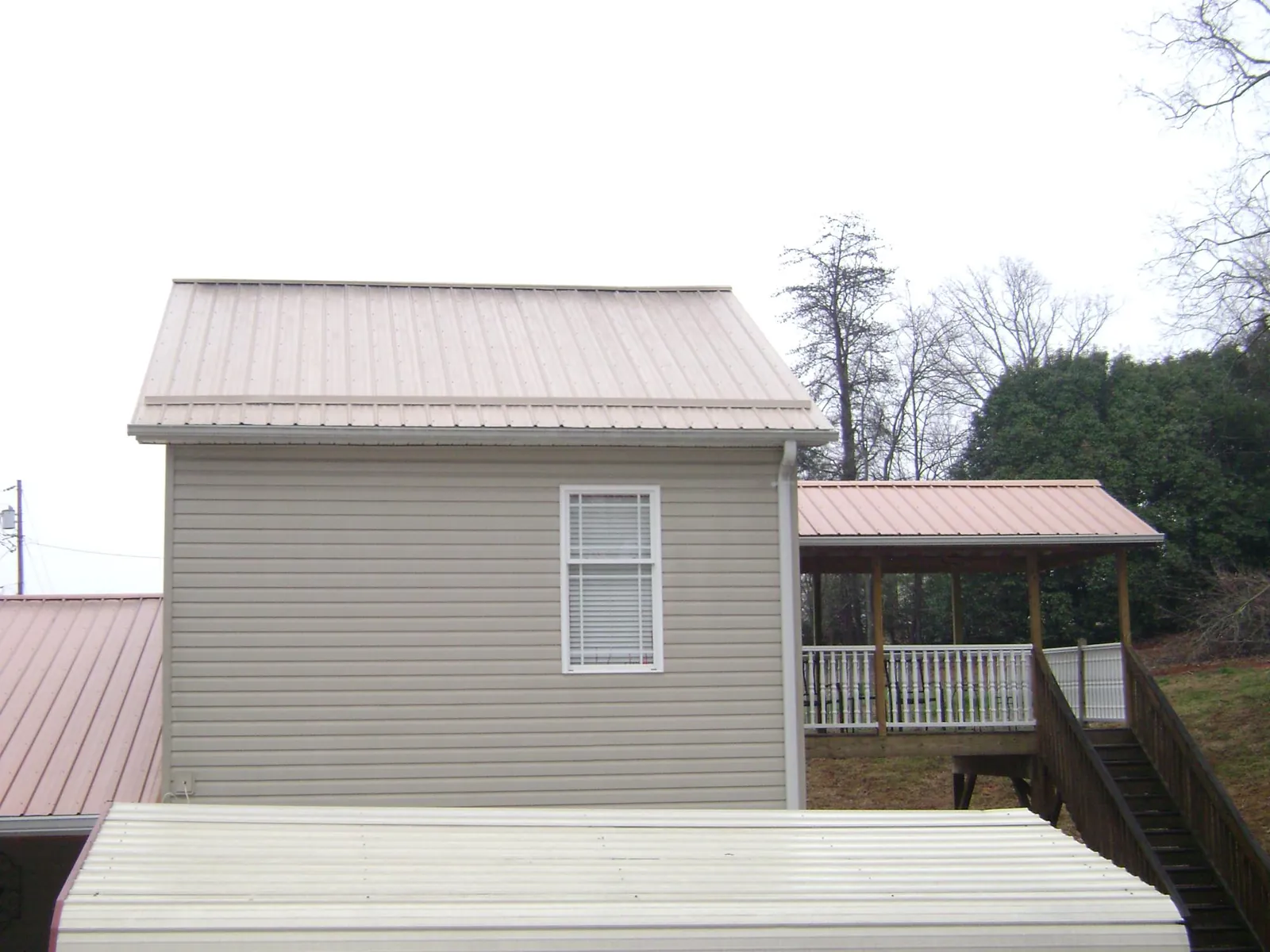 Tan metal roofs on a two story addition and attached porch, from a Roof Replacement job in Grimesland